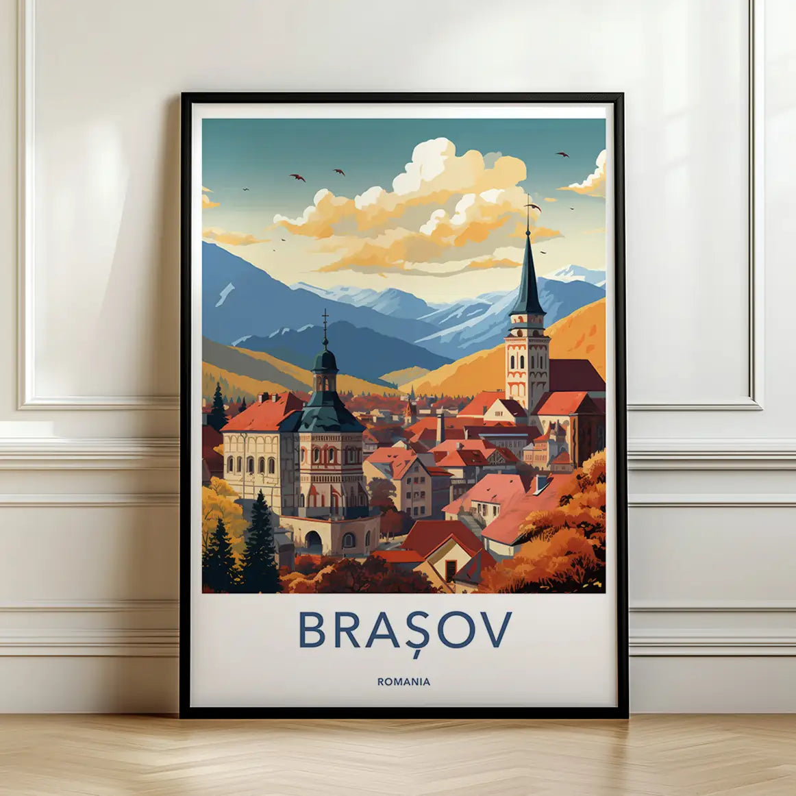 Framed travel poster of Brasov's historic town square and orange roofs against mountain peaks leaning against a white wall.