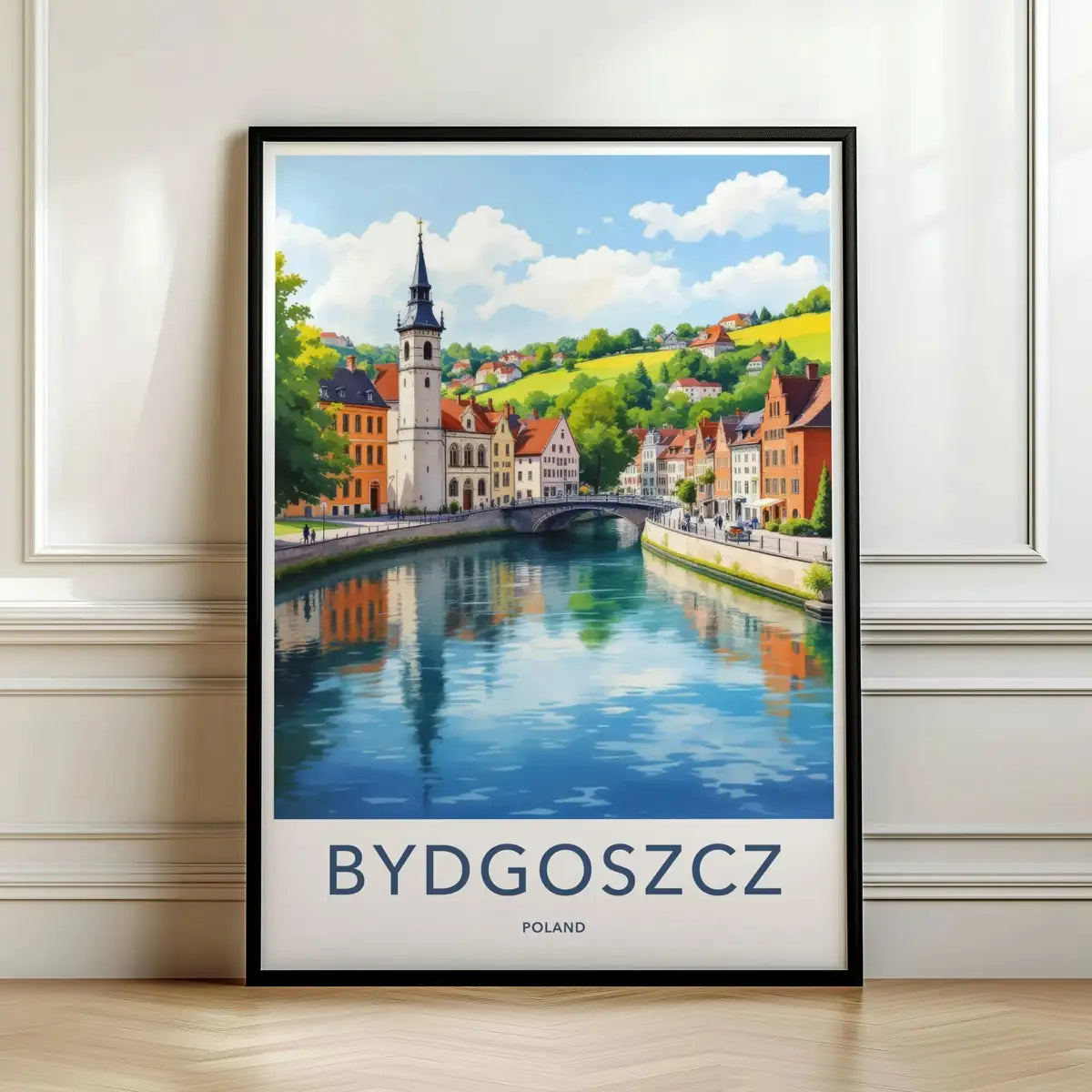 Framed travel poster of Bydgoszcz's colorful riverside buildings and bridge leaning against a white wall.