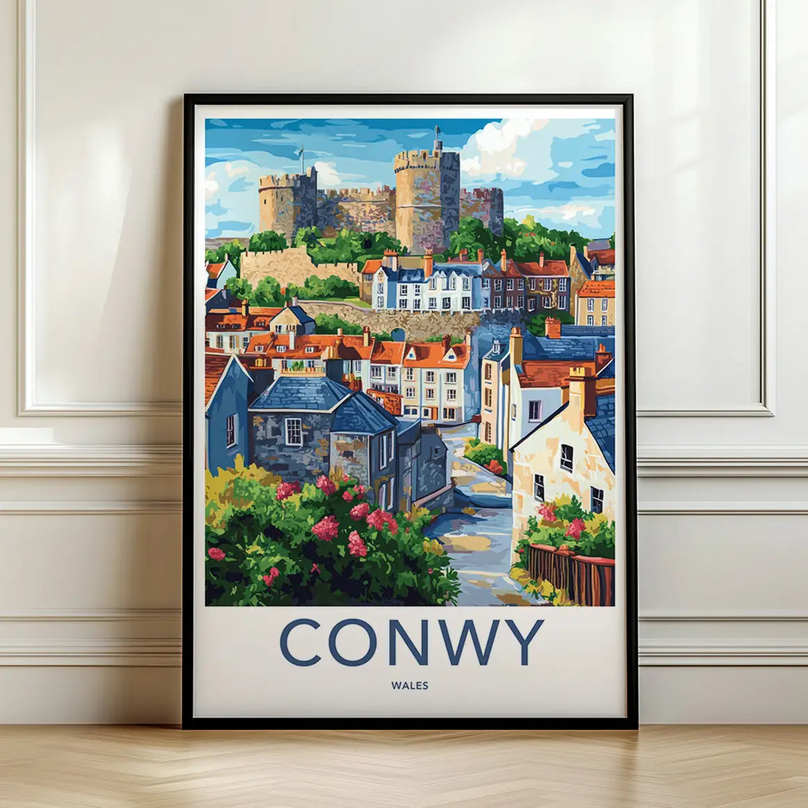 Framed travel poster of Conwy Castle and colorful coastal houses leaning against a white wall.