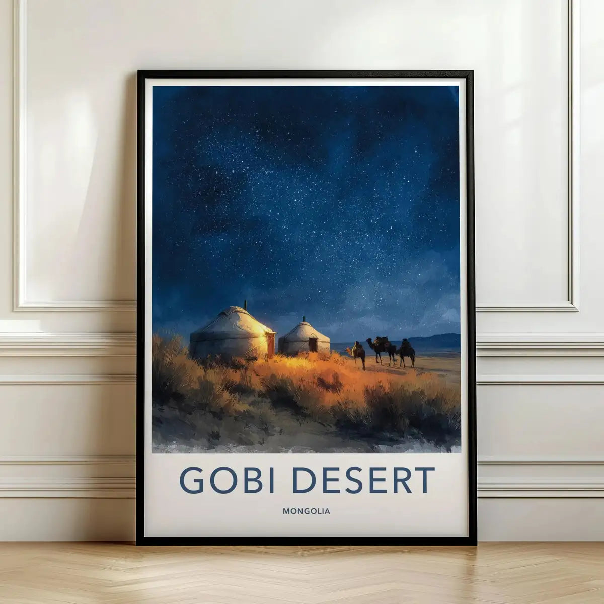 Framed travel poster of the Gobi Desert with yurts and camels under a starry night sky leaning against a white wall.