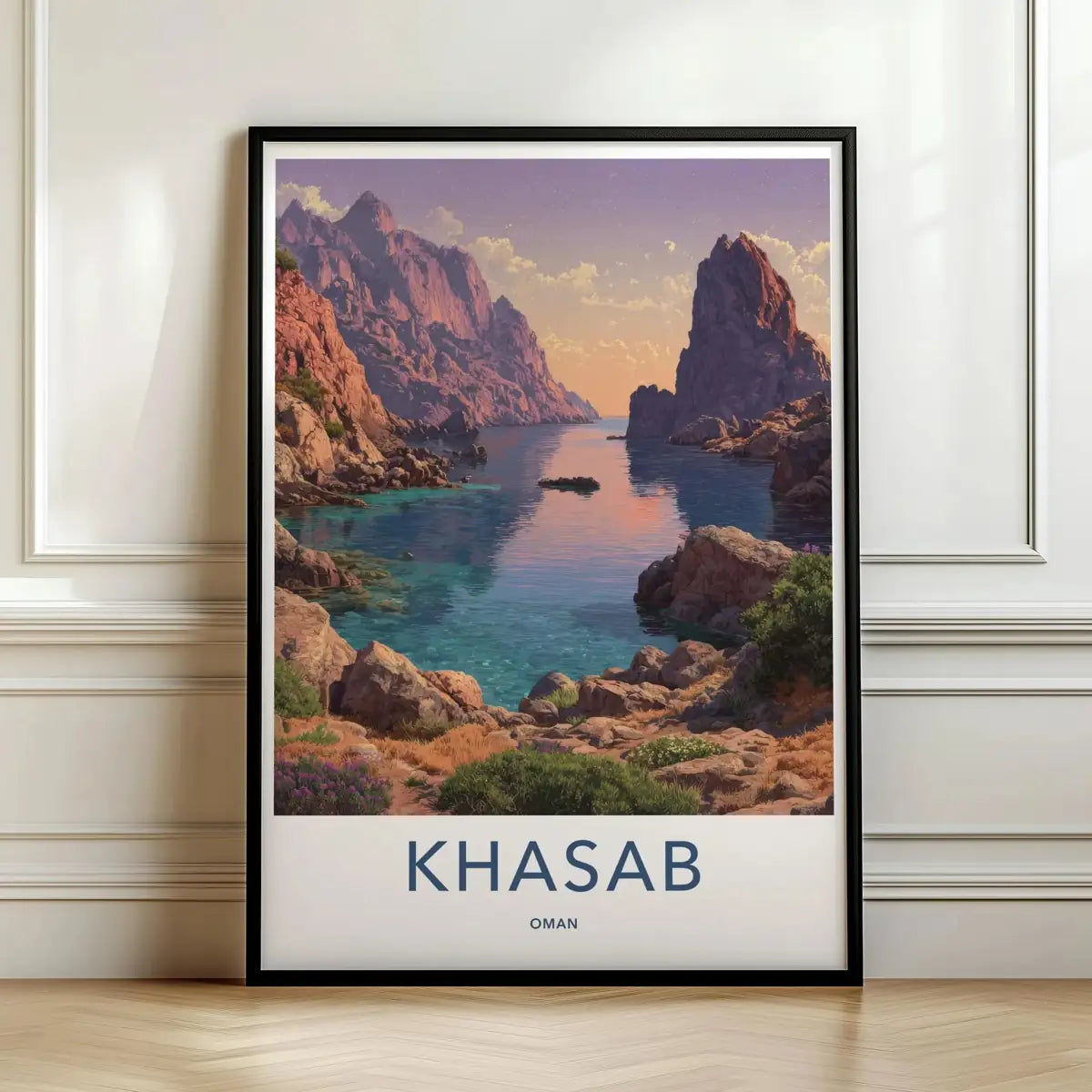 Framed travel poster of Khasab's steep coastal fjords and calm waters at sunset leaning against a white wall.
