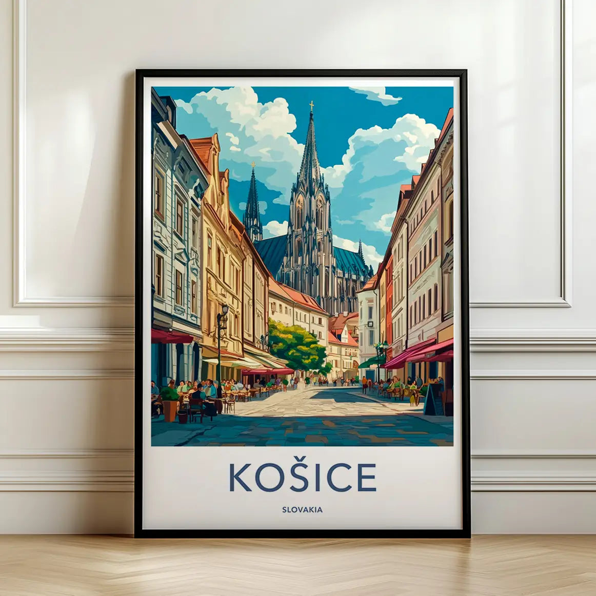 Framed travel poster of Kosice's gothic cathedral and colorful city street leaning against a white wall.