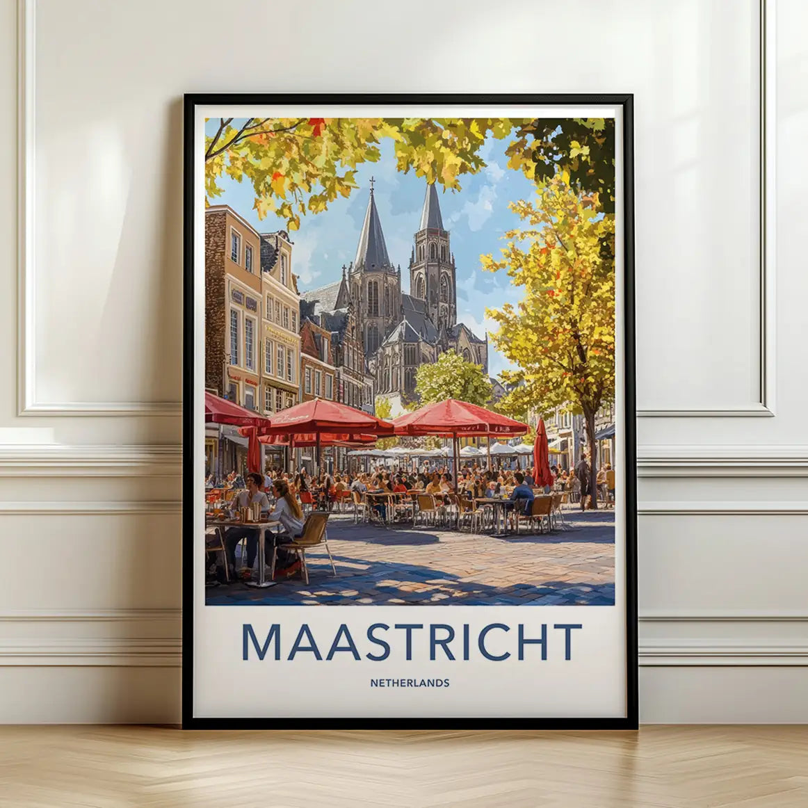 Framed travel poster of Maastricht's historic architecture and an outdoor cafe scene leaning against a white wall.