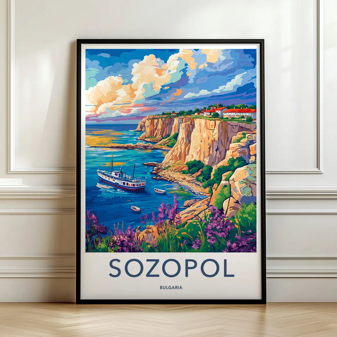 Framed travel poster of Sozopol's vibrant coastal cliffs, purple wildflowers, and a boat in the blue sea leaning against a white wall.