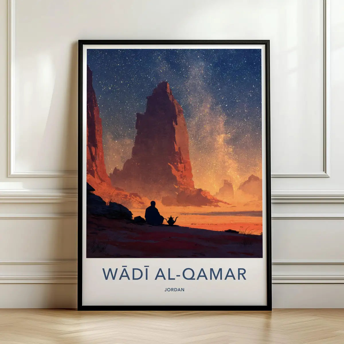 Framed travel poster of Wadi Al-Qamar's desert rock formations under a starry night sky leaning against a white wall.