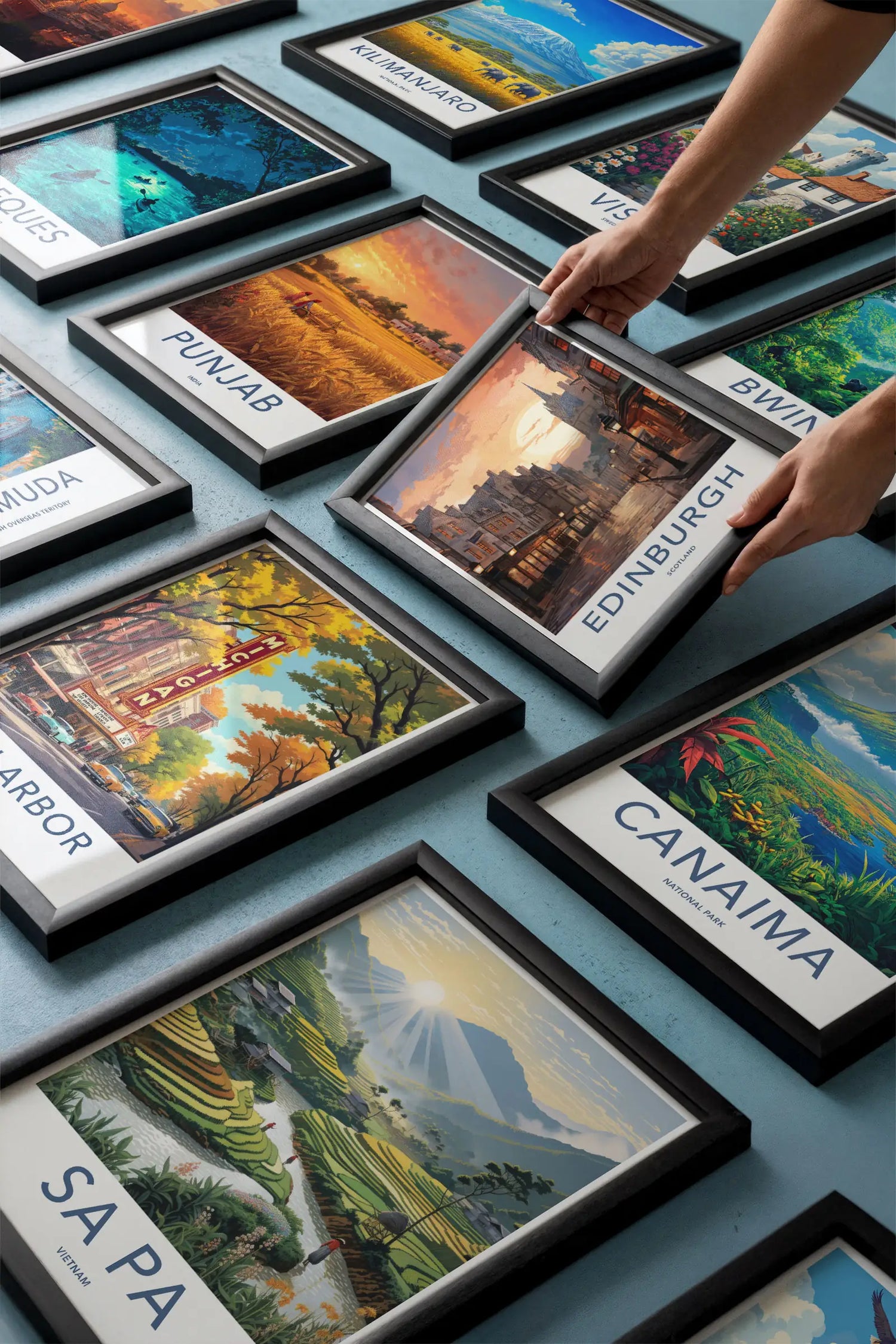 Hands arranging multiple framed vintage travel posters including Edinburgh and Sa Pa showcasing Artfultravelpast gallery.