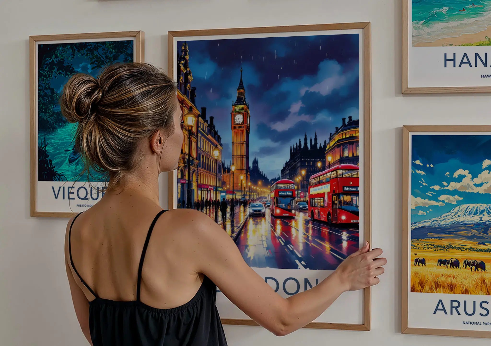 Woman hanging a framed London Big Ben travel poster on a gallery wall surrounded by global destination prints.