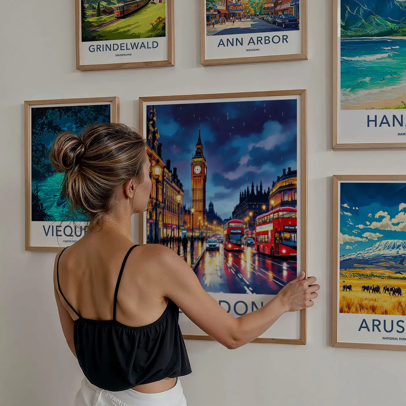 Woman hanging a framed London Big Ben travel poster on a gallery wall surrounded by global destination prints.