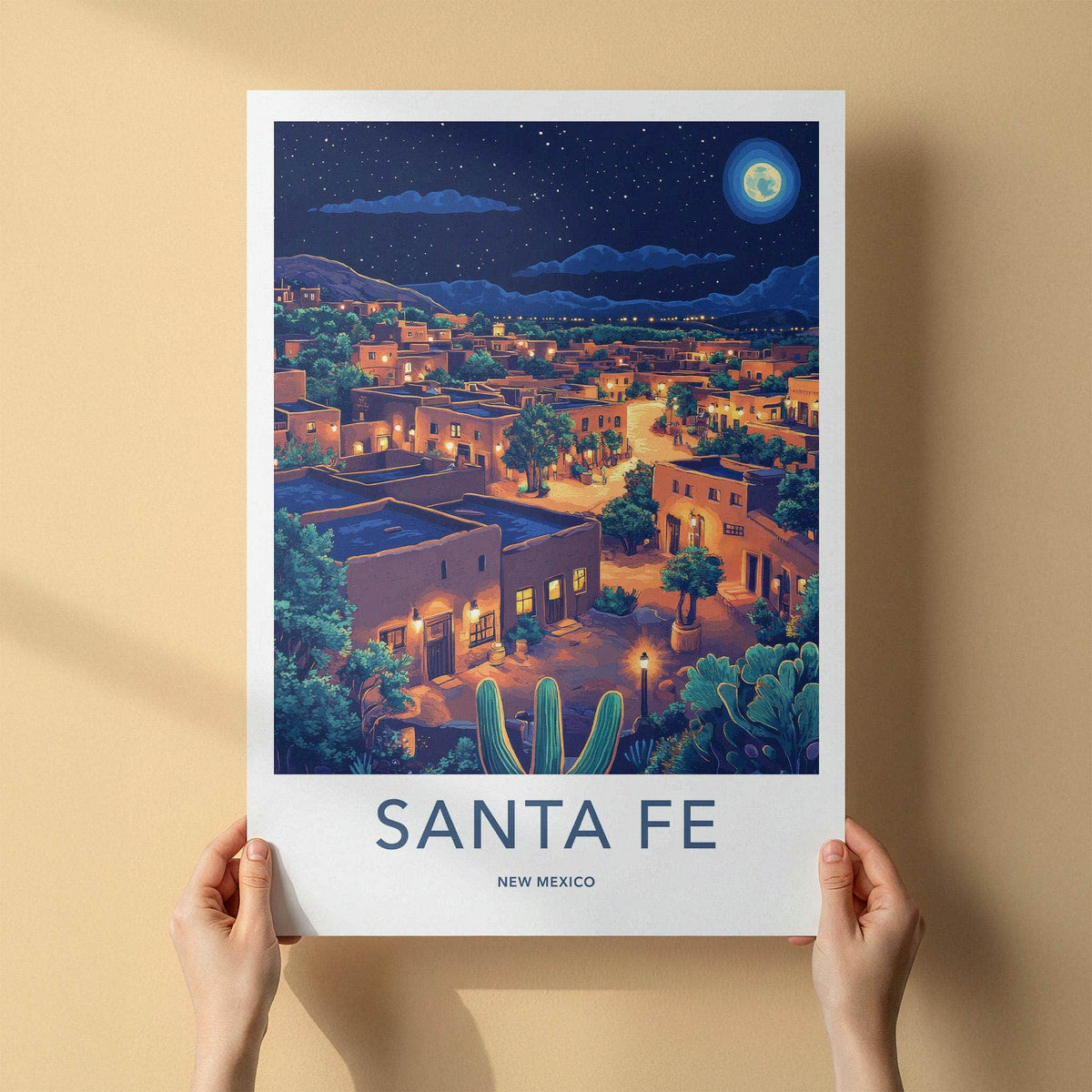 A person holds a vertical travel poster of Santa Fe, New Mexico, showing a stylized night view of the town with adobe buildings, cacti, and a starry sky. The poster has a white border with the text 'SANTA FE NEW MEXICO' at the bottom.
