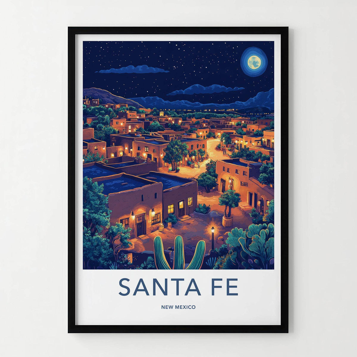 A framed travel poster of Santa Fe, New Mexico, featuring a stylized night illustration of the town with adobe buildings, cacti, and a full moon, presented in a black frame.