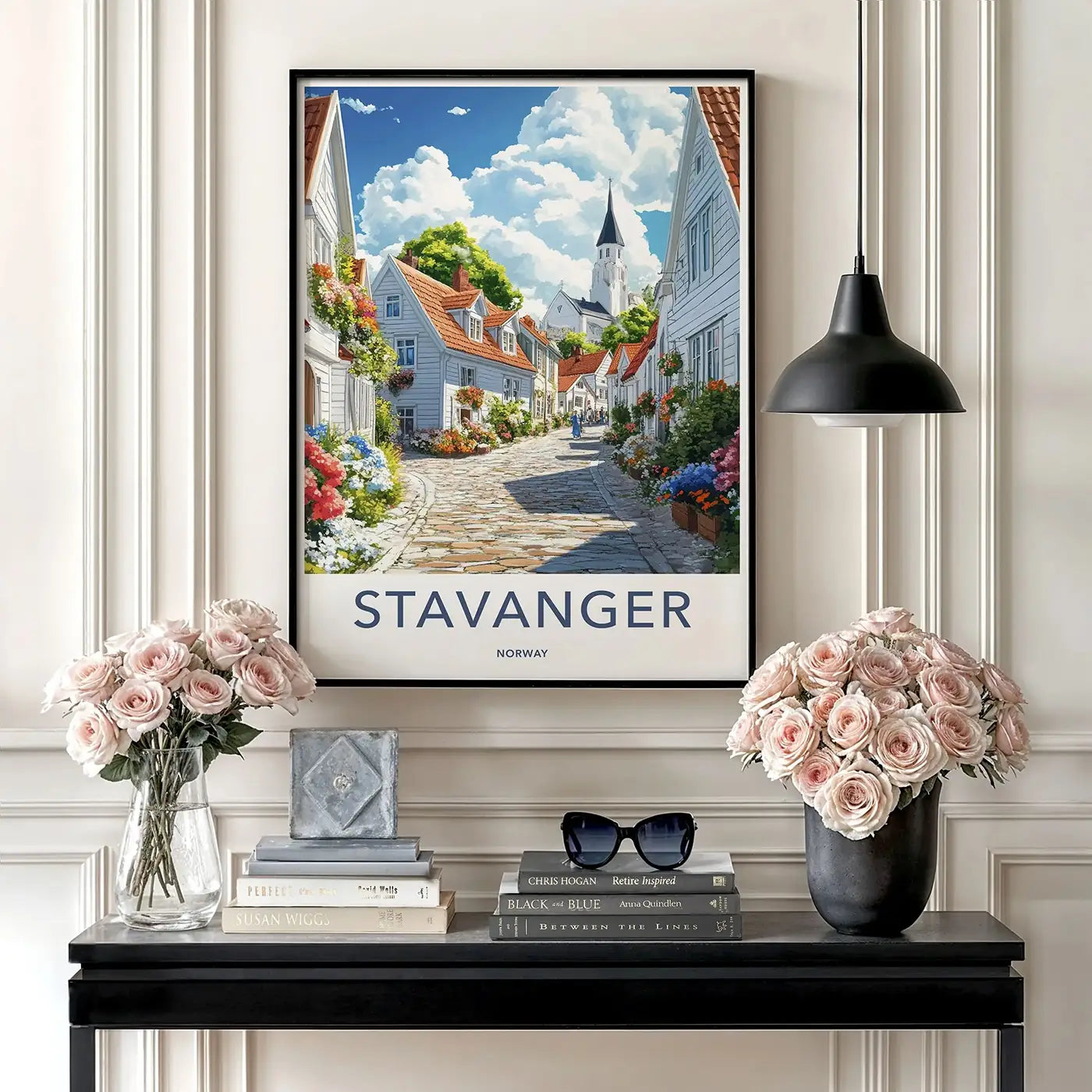 Framed travel poster of Stavanger Norway hanging above a black console table decorated with pink roses in a gallery setting.